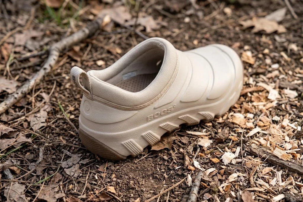 A beige sneaker shoe lying on a forest floor covered with dry leaves, twigs, and dirt.