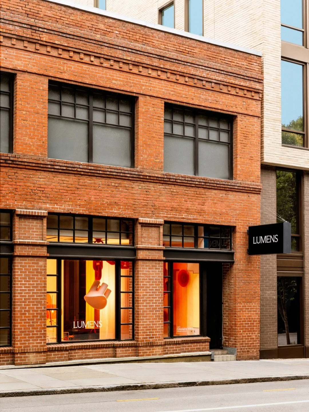 Exterior view of a brick building with storefront windows displaying lighting fixtures and a sign that reads 'LUMENS'.