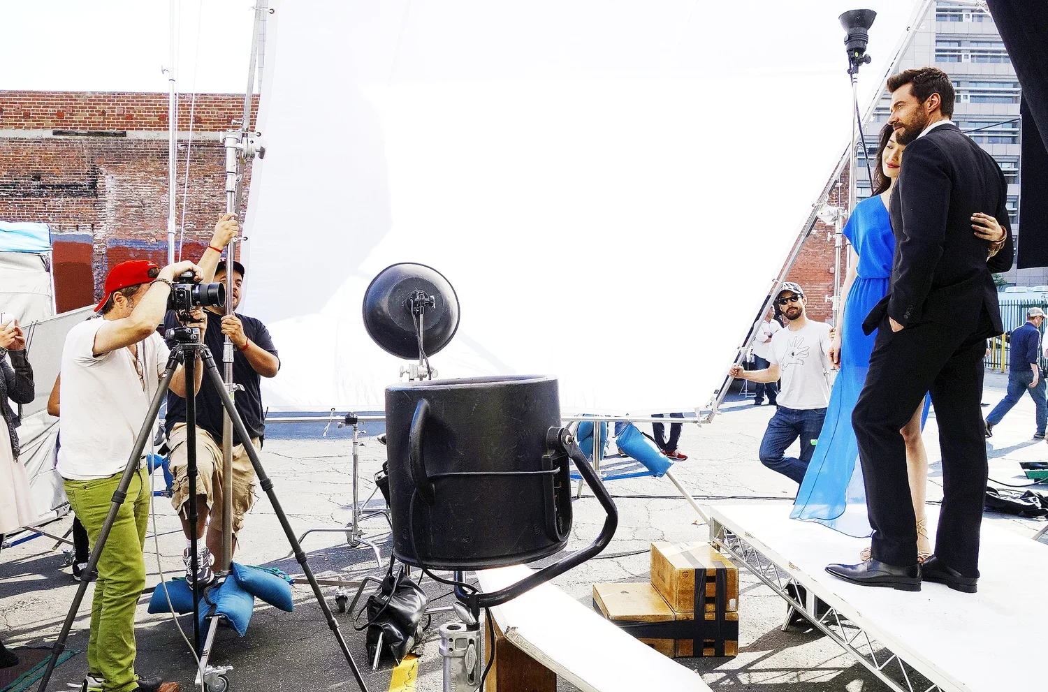 Behind the scenes of a photoshoot featuring a man and woman on a platform, with photographers and crew members adjusting equipment and lighting.