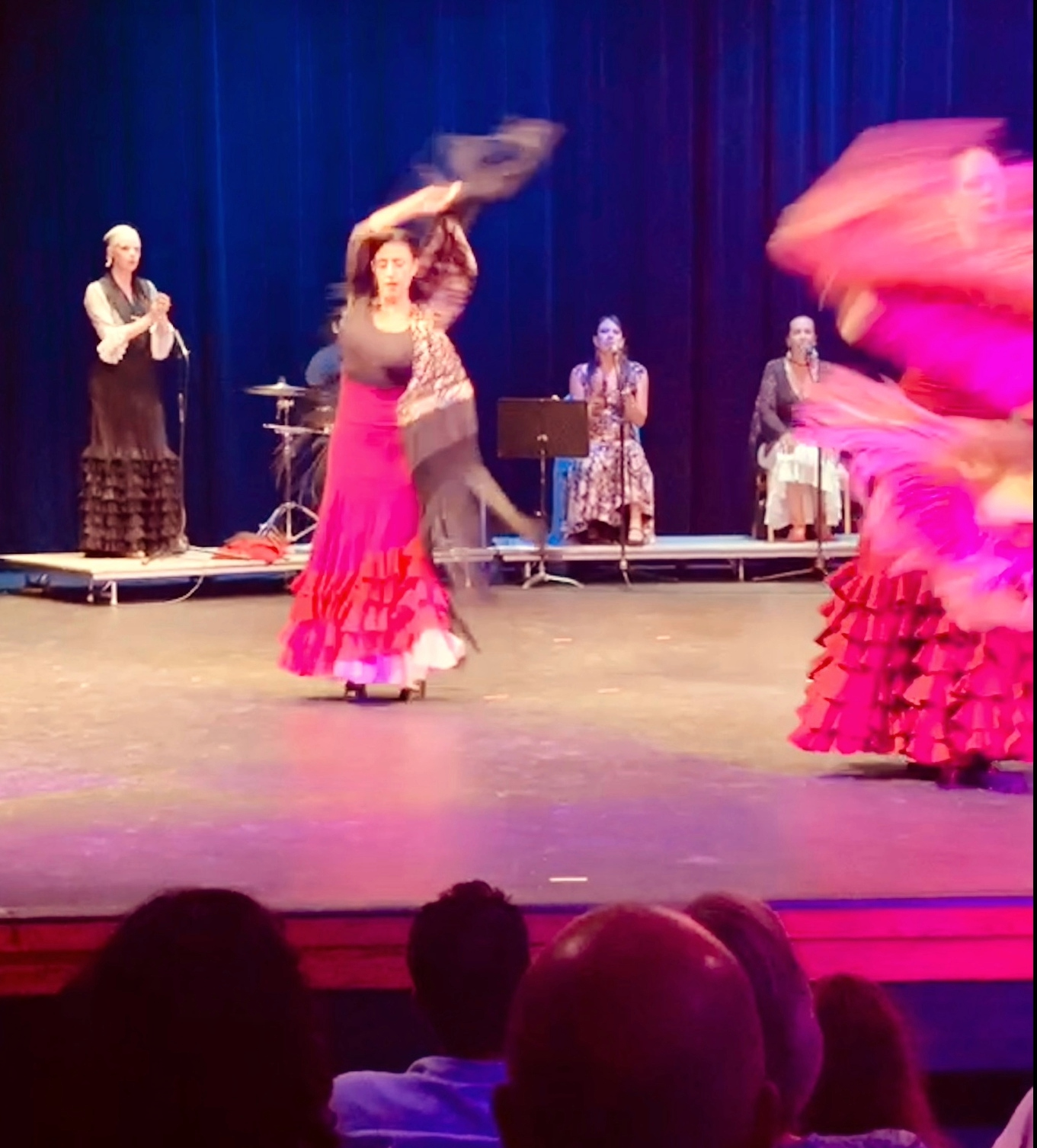 Flamenco dancers performing on stage with musicians in the background, wearing traditional colorful dresses with ruffles.