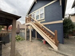 The rebuilt staircase, new wood railings and updated siding bring the home’s exterior transformation into view. These improvements connect the upper entrance to the patio and form part of the larger fence and gate project.