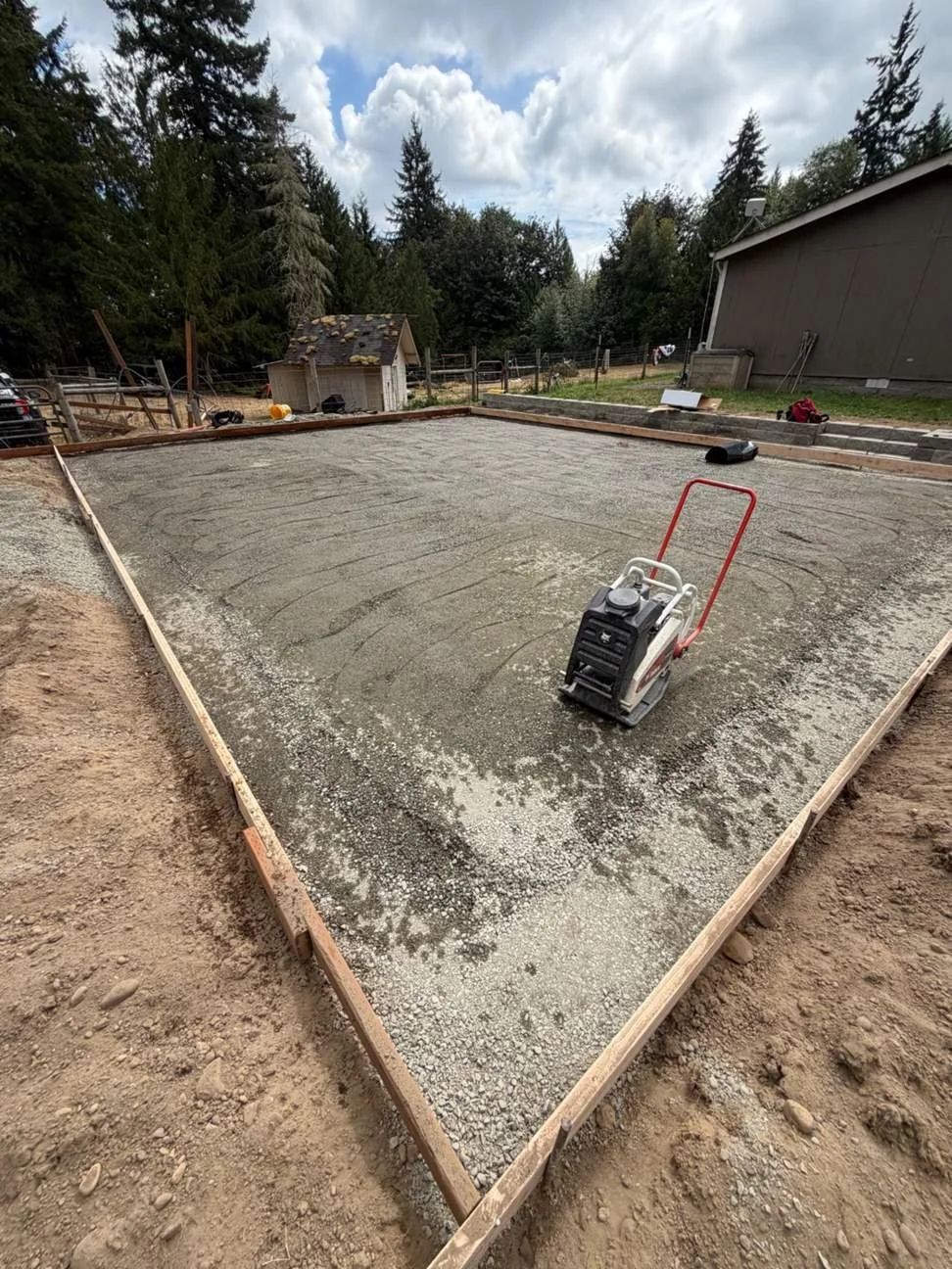 Work begins with preparing the gravel base inside the wood forms. A plate compactor is used during this stage before the barrier and reinforcing steel are added.