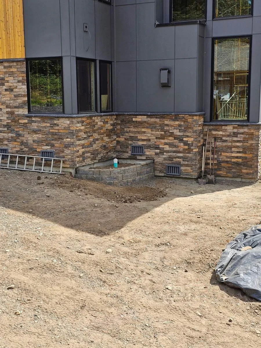 This exterior project combines stacked-stone veneer with dark siding and a small curved retaining wall beside the foundation. The stonework wraps around the home’s corners and beneath the windows, adding texture to the exterior.