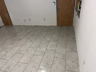 The new tile floor extends across the room in a coordinated staggered layout. With the leveling clips removed, the flooring portion is taking shape ahead of baseboards and the remaining room finishes.