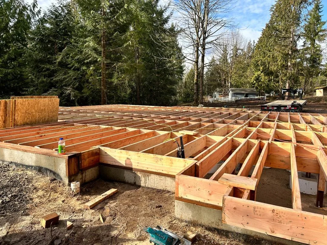 Wood floor joists and blocking installed over a concrete foundation, showing the framing stage before subfloor placement.