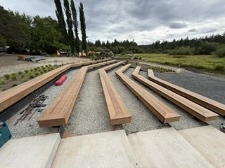 Wood seating boards now cover the angled bench frames, bringing the gathering area into shape. Multiple rows provide seating with gravel aisles between them.