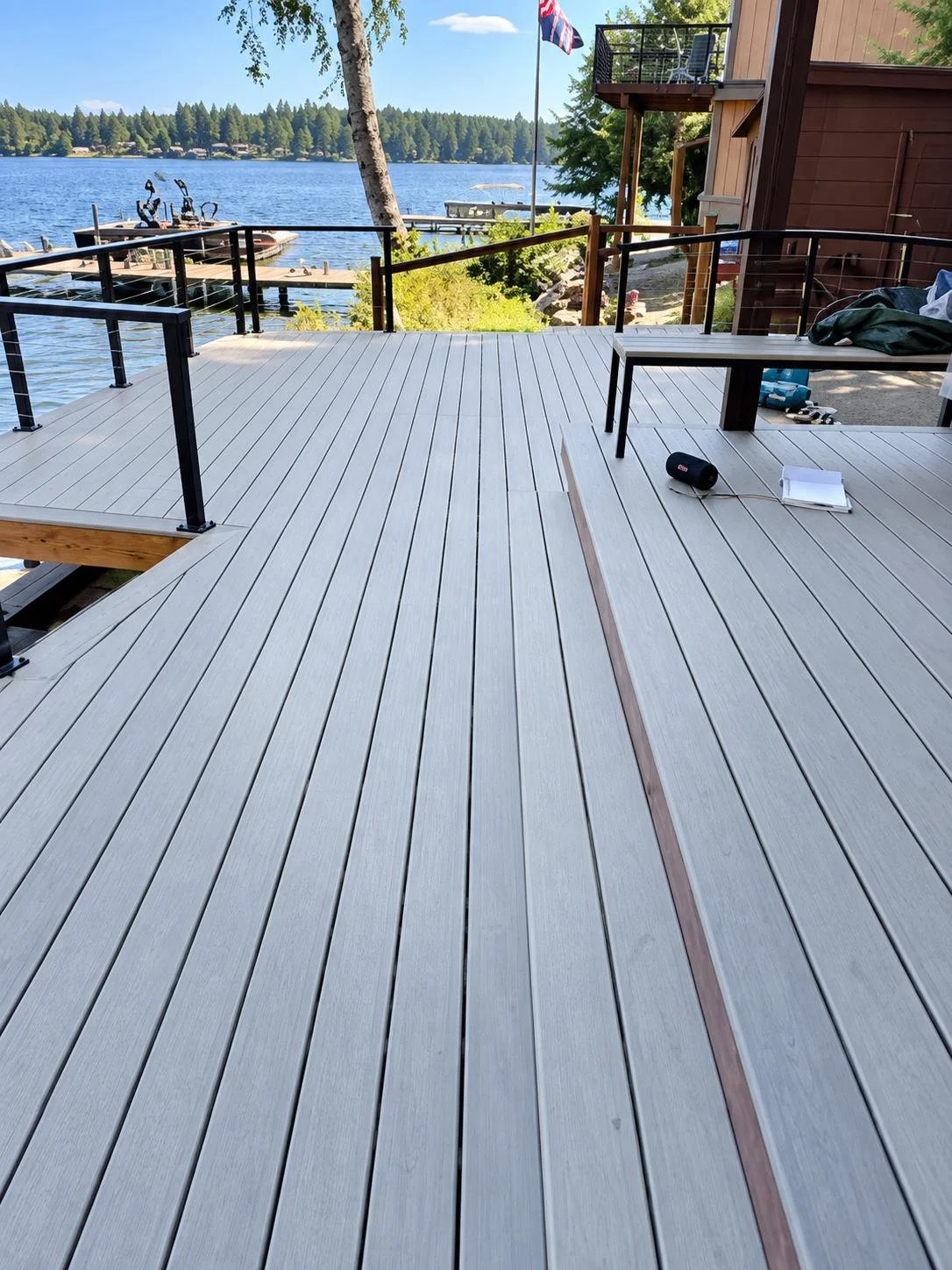 Deck Installation and Repair featuring gray deck boards, black railings and steps connecting a waterfront home to its yard.