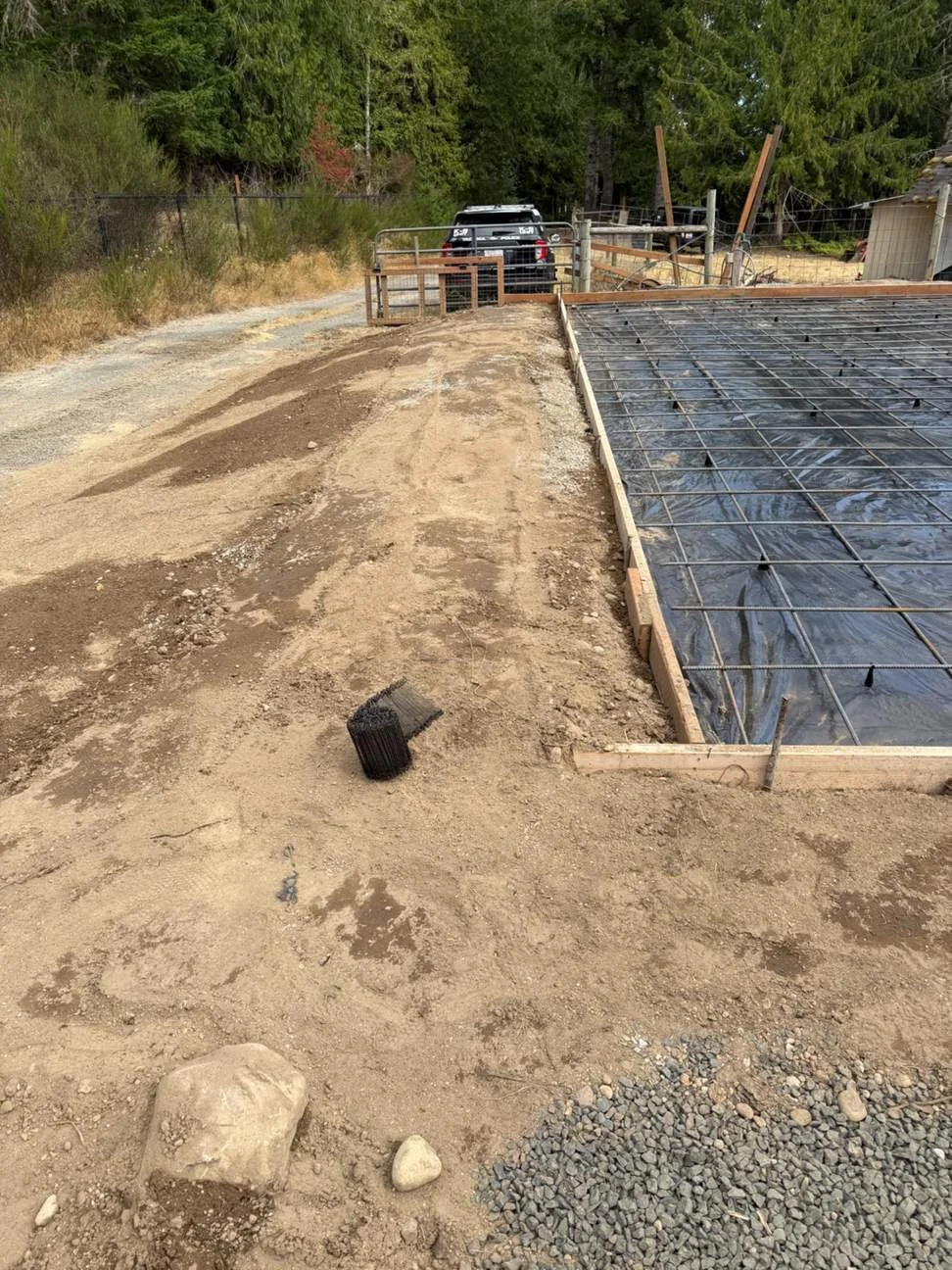 The prepared slab area sits alongside the surrounding graded ground, with perimeter forms defining its shape. This view captures the site conditions and reinforcement work before the concrete pour.