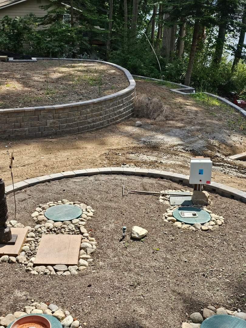 The terraced yard combines a taller curved retaining wall with lower block borders. Coordinated blocks and capstones connect the different sections as the surrounding landscape work progresses.