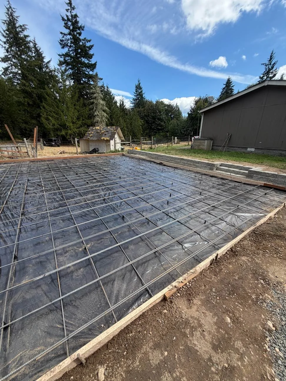 A grid of reinforcing steel is installed over the black barrier within the slab forms. This stage brings the base preparation and reinforcement together ahead of concrete placement.