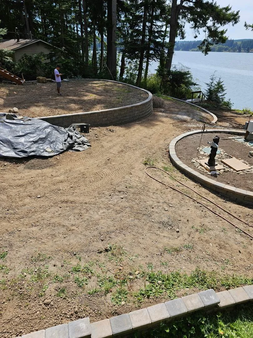 This waterfront yard project uses curved block retaining walls to create distinct levels across the sloping property. Capped wall sections define the upper yard and follow the landscape toward the water.