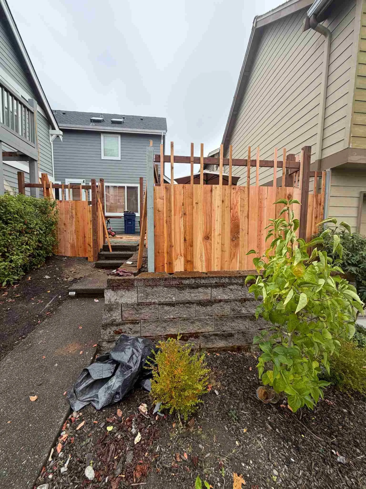 Wood privacy fence installation in progress beside residential steps, with exposed upper framing and new boards.