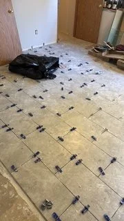 Rectangular floor tiles are being installed in a staggered pattern, with leveling clips in place as the work progresses. This stage focuses on tile placement and consistent joints before grouting and finishing.