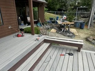 The crew is fitting deck boards and contrasting trim around the steps between levels. Tools and materials remain on site as the stair treads and surrounding edges take shape.