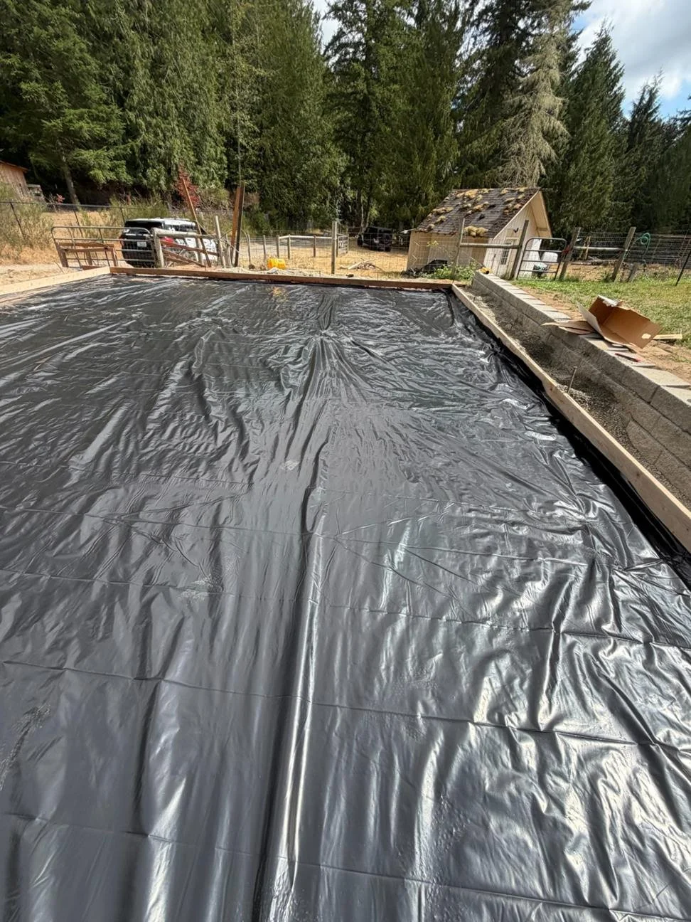 Black sheeting covers the prepared base within the wood forms. This layer is installed before the reinforcing steel as the project moves toward concrete placement.