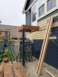 Construction begins with new posts and framing for the upper landing while siding work progresses around the doorway. This platform will connect the home’s entrance to the rebuilt staircase.