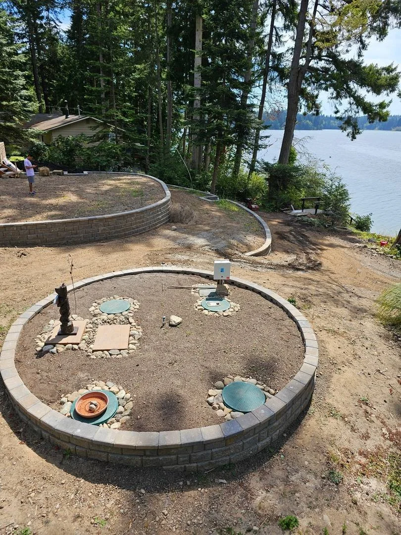 This portion of the project adds a circular block border around an existing utility area. Its curved layout complements the nearby retaining walls while leaving access covers exposed.