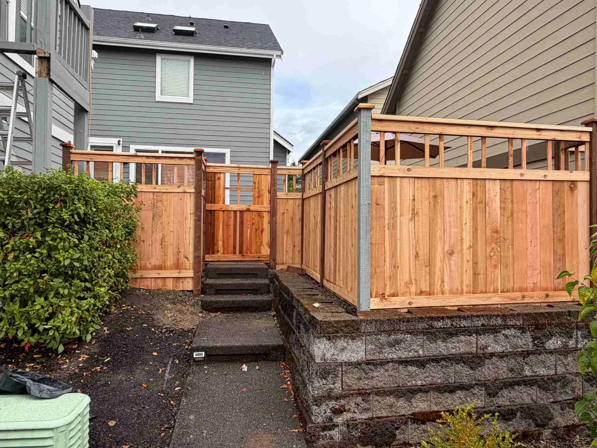 Wood privacy fence and matching gate with decorative upper slats beside residential steps and a retaining wall.