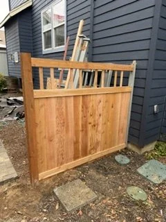 The fence takes shape with vertical wood boards and an open decorative top. Its design adds privacy beside the home while matching the gate being installed as part of the project.