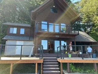 A wider view brings the deck, central staircase and railings into one connected layout. The updated outdoor space spans the home’s waterfront exterior and provides access between the house and yard.