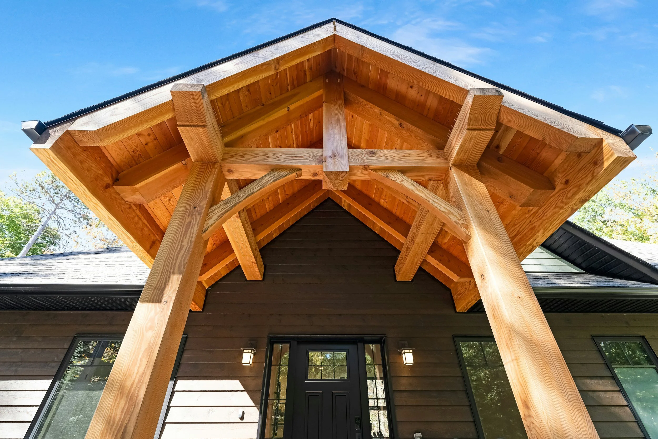 Front view of a modern house with wooden porch columns and a gabled roof, against a clear blue sky.