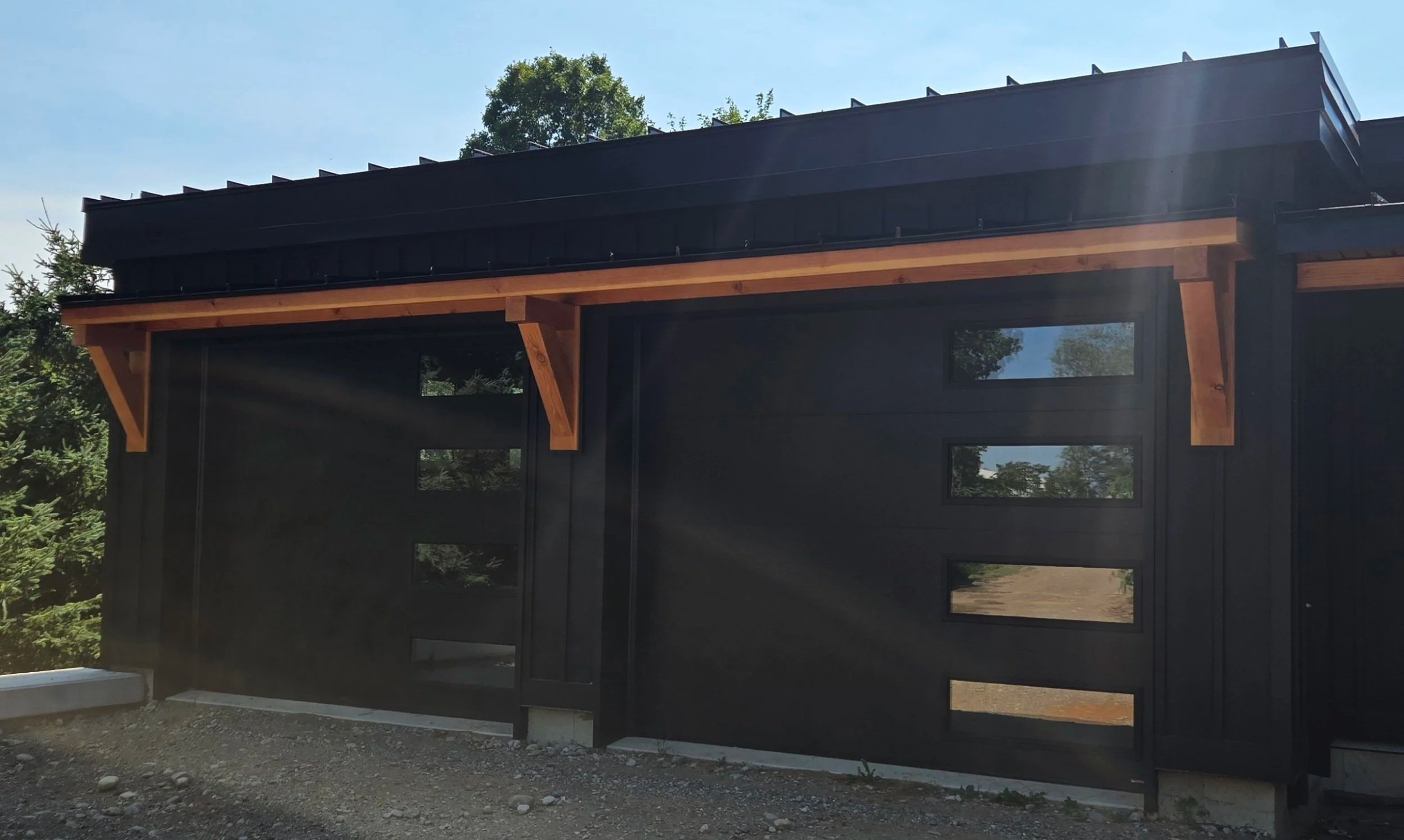 A modern black wooden building with horizontal siding and rectangular windows, featuring a sloped metal roof with black shingles.