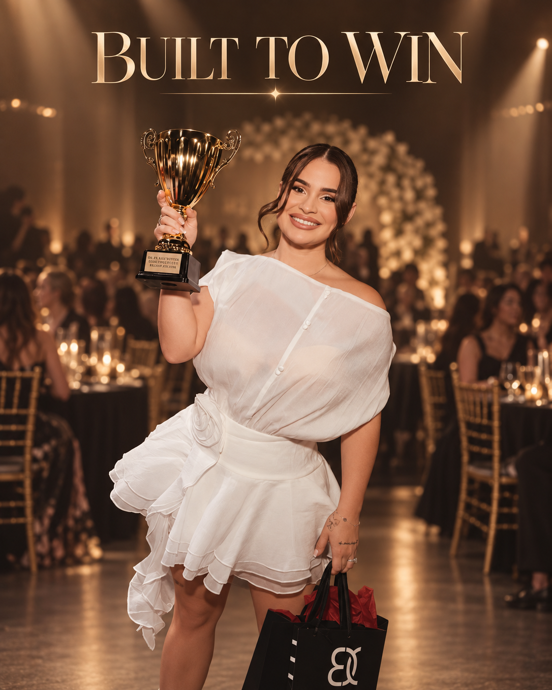 A woman in a white dress smiling while holding a gold trophy at an awards ceremony with the words 'Built to Win' displayed behind her.
