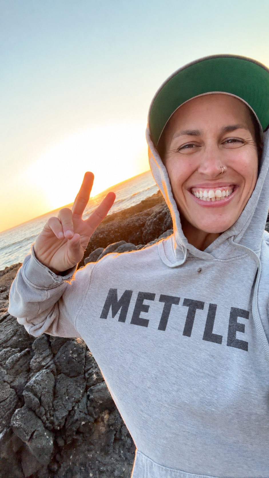 Jacqui smiling at the coast in a METTLE hoodie.