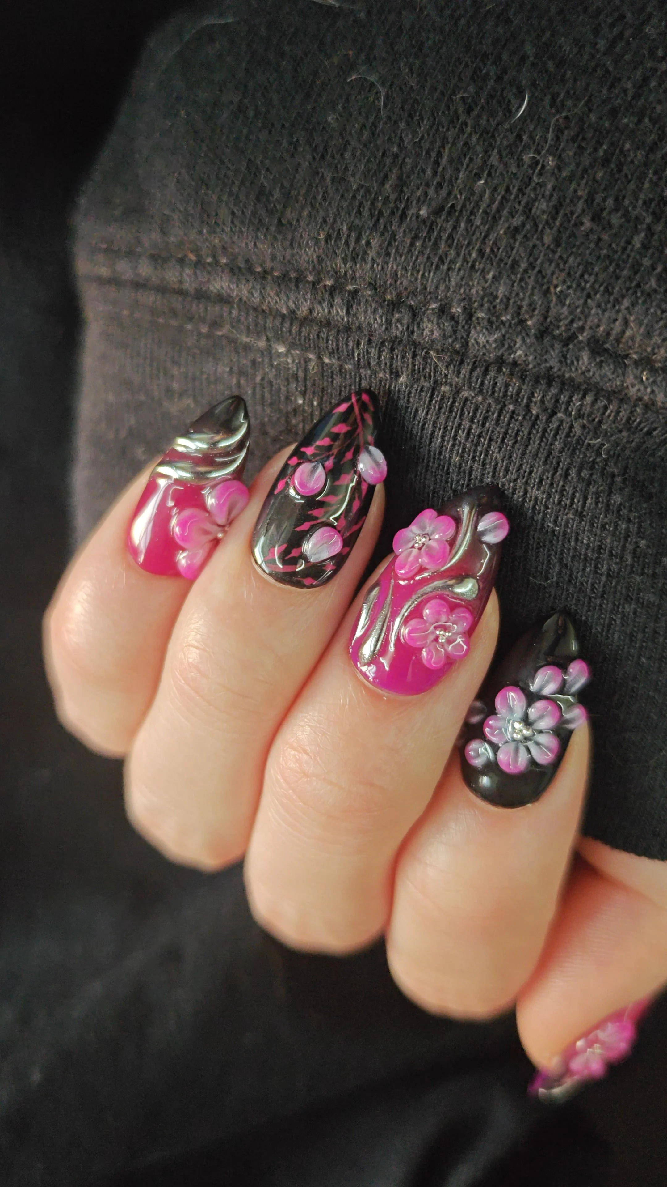 Close-up of a hand with pink and black floral nail art, resting on dark fabric.