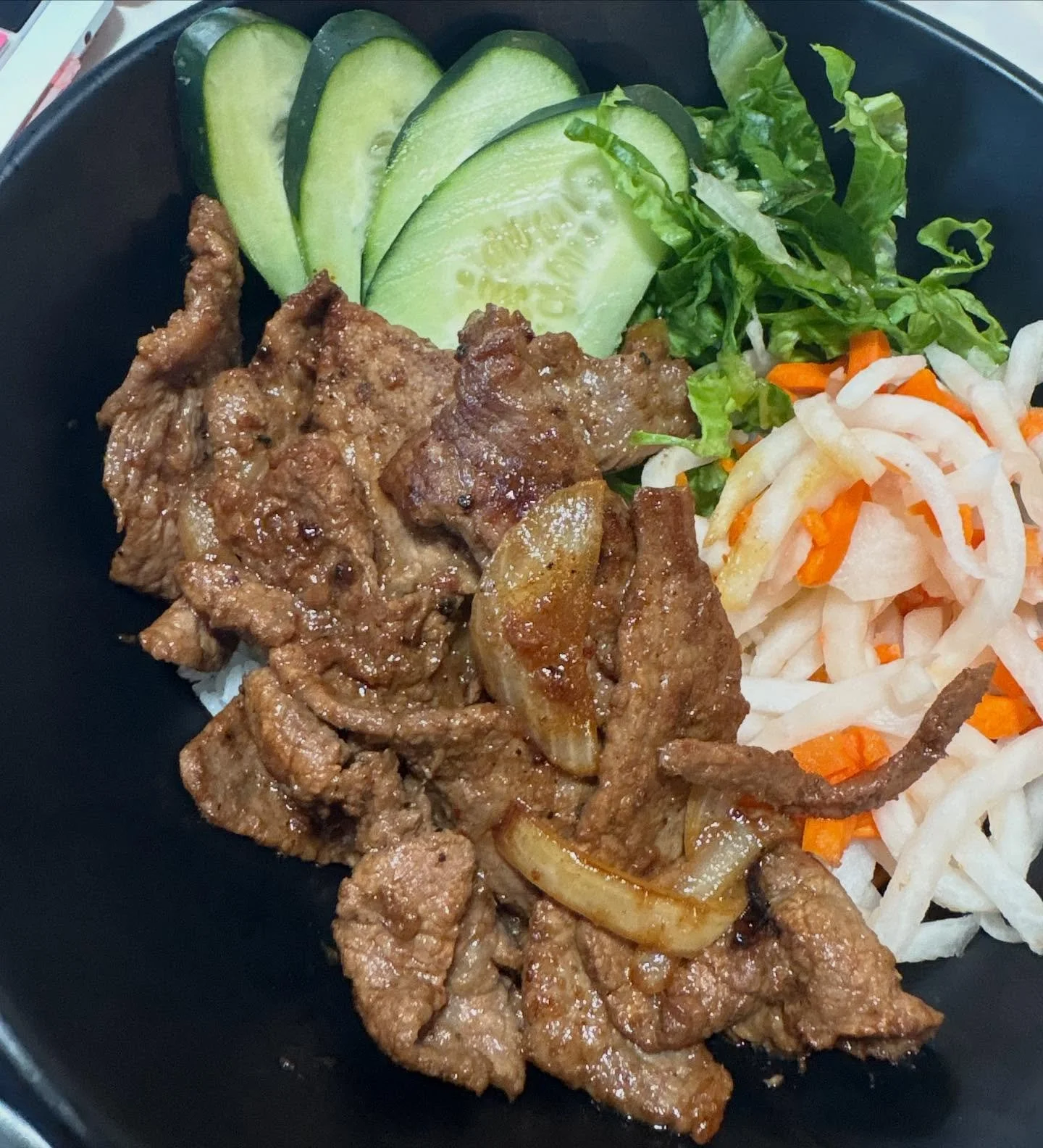 Plate of sliced cucumbers, shredded lettuce, and shredded cabbage with carrots, accompanied by cooked beef with onions.