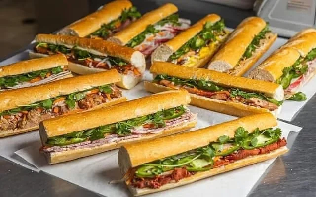 Multiple submarine sandwiches filled with various meats, lettuce, tomatoes, and other toppings, served on hoagie rolls.