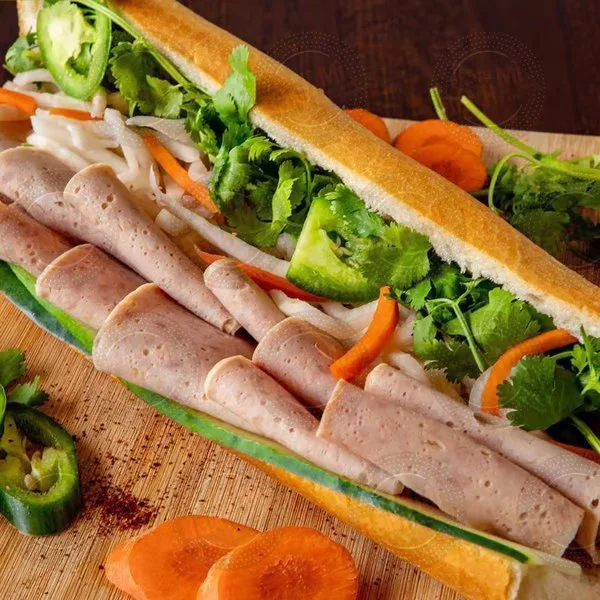 A Vietnamese banh mi sandwich with sliced turkey, fresh cilantro, jalapeño slices, pickled carrots, cucumber, and lettuce on a baguette.
