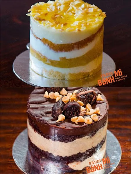 Two layered cakes, one with yellow and white layers topped with pineapple, and the other with chocolate, caramel, and nuts, both on silver bases.