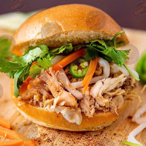 Close-up of a sandwich with shredded chicken, cilantro, jalapeño slices, and shredded carrots on a bun.