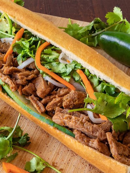A Vietnamese banh mi sandwich with shredded meat, fresh vegetables, and herbs in a baguette.