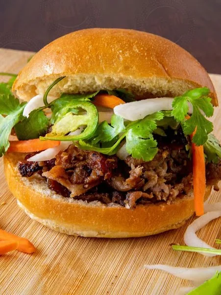 Beef sandwich in a bun with fresh lettuce, sliced jalapenos, and shredded onions.
