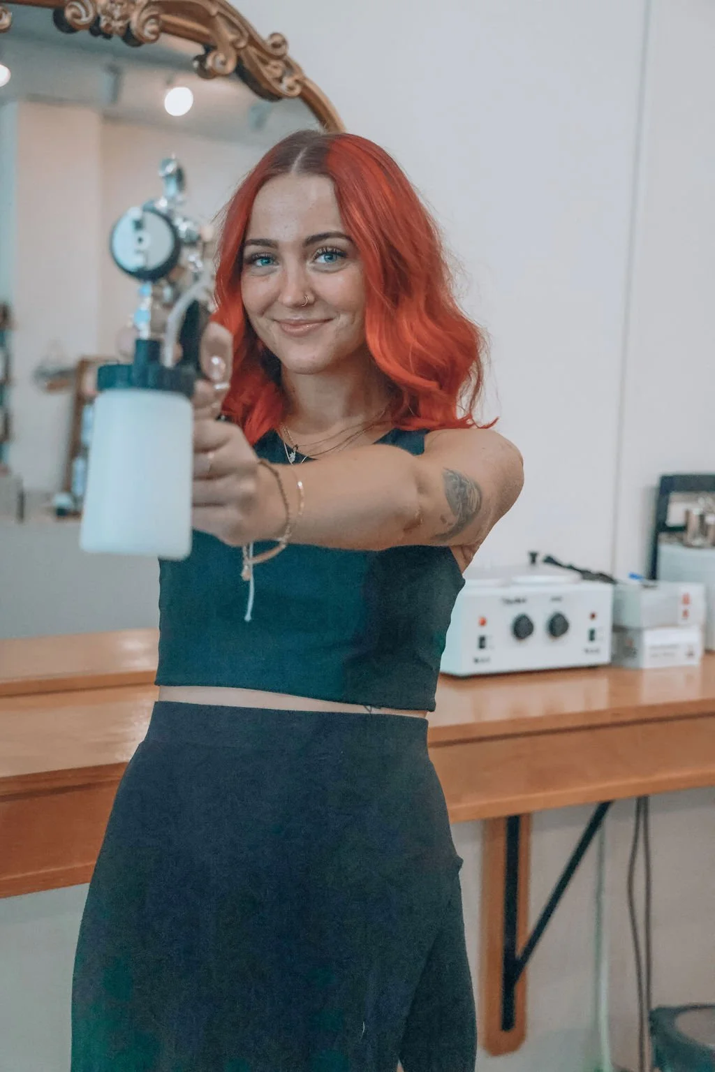A young woman with pink hair and tattoos holding tanning gun. Bee Smooth tanning