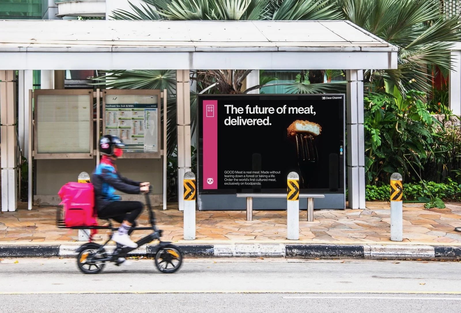 A person riding a bicycle past a bus stop with an advertisement saying "The future of meat, delivered" and an image of a meatless chicken nugget.
