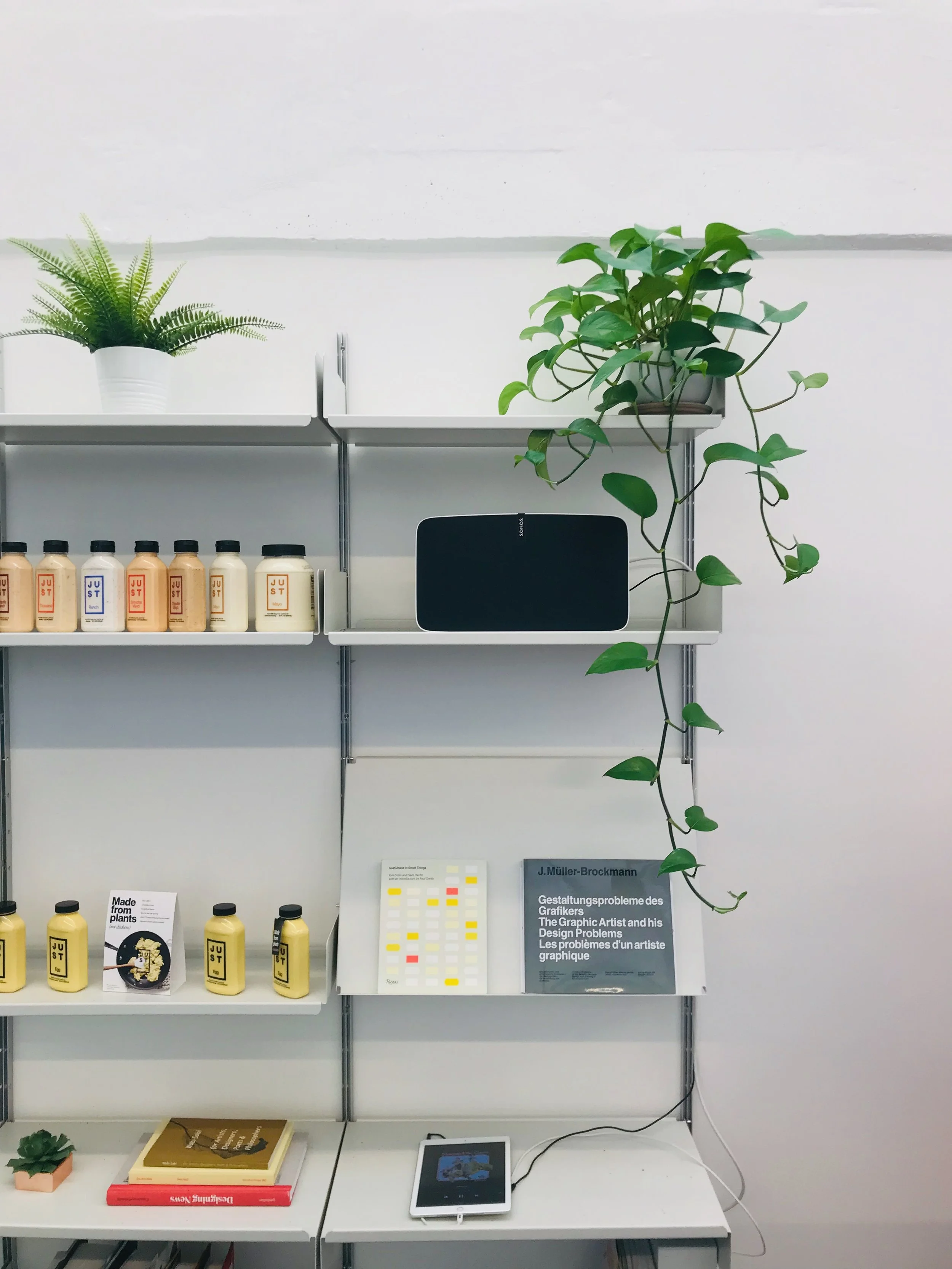 Books, plants, and electronic devices on white shelves and table at a display or office space.