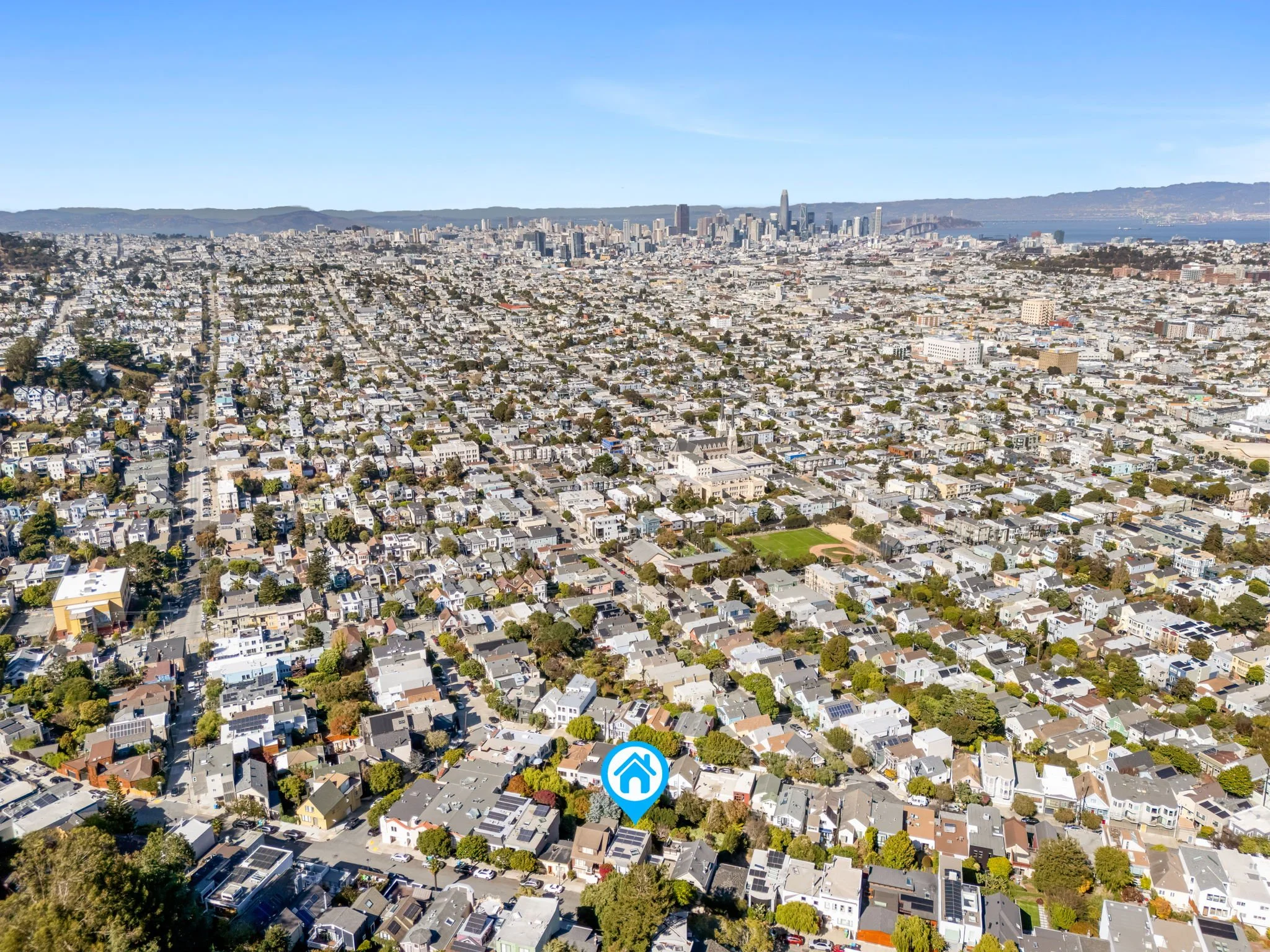 Aerial view of a densely populated city with a mix of residential houses and tall skyscrapers in the downtown area, with hills in the background and the bay in the distance.