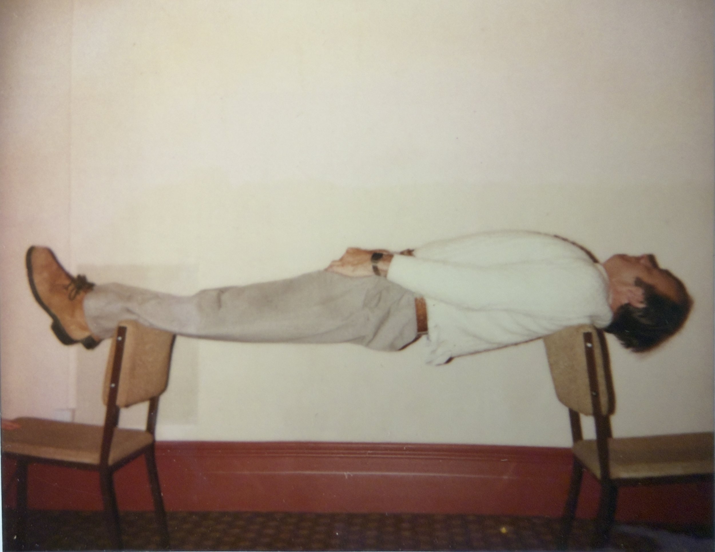 A person hypnotised dressed in a white jacket, light-colored pants, and brown boots elevating on a chair.
