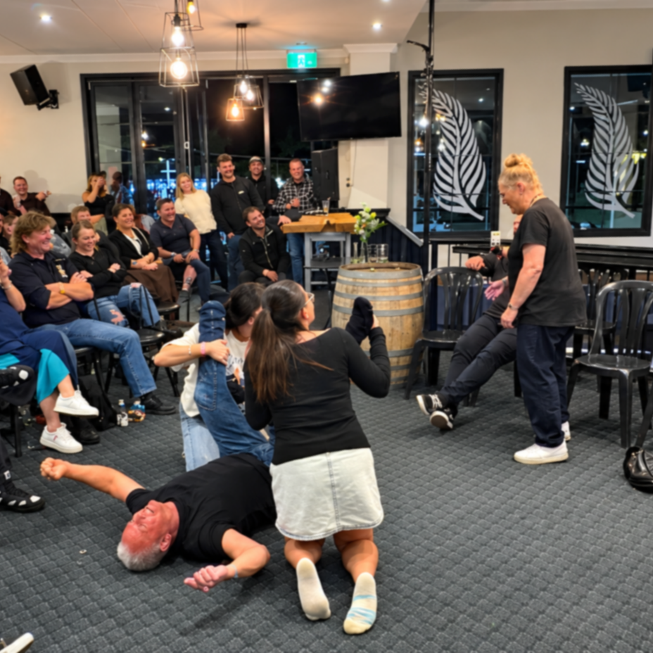 People attending a hypnotist show in a warmly lit restaurant or bar, with some on a stage, laughing and enjoying entertainment.