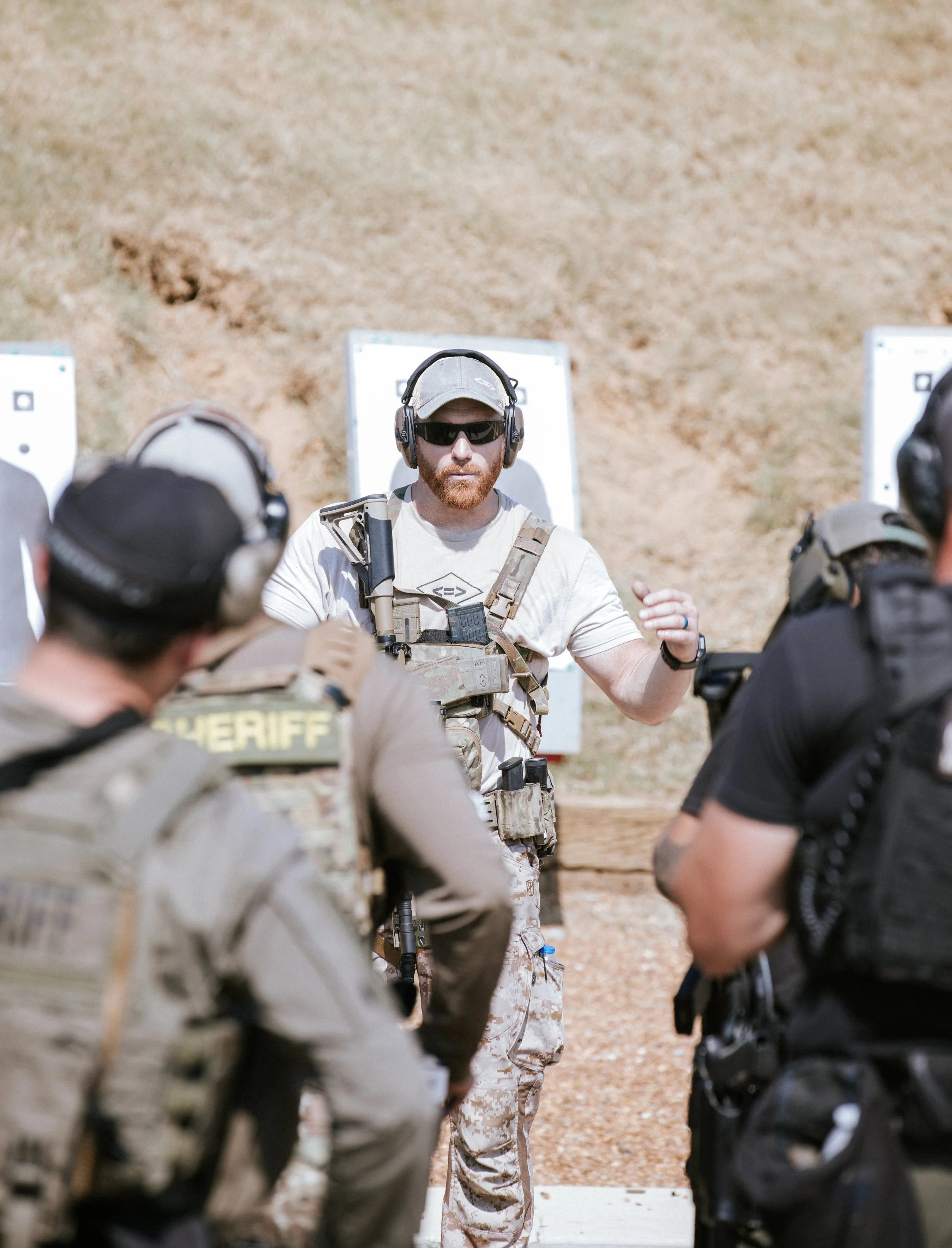 An instructor in military gear giving instructions to a group of soldiers during a training exercise outdoors.