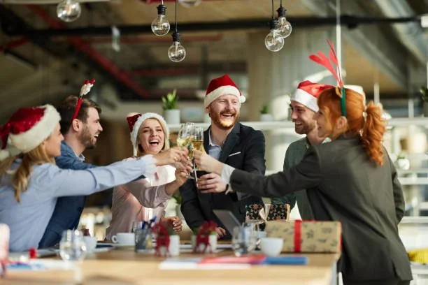 Group of friends wearing Christmas hats and accessories celebrating with drinks in a cozy, decorated space.