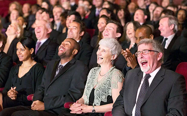 An audience seated in a theater, laughing and enjoying a performance.