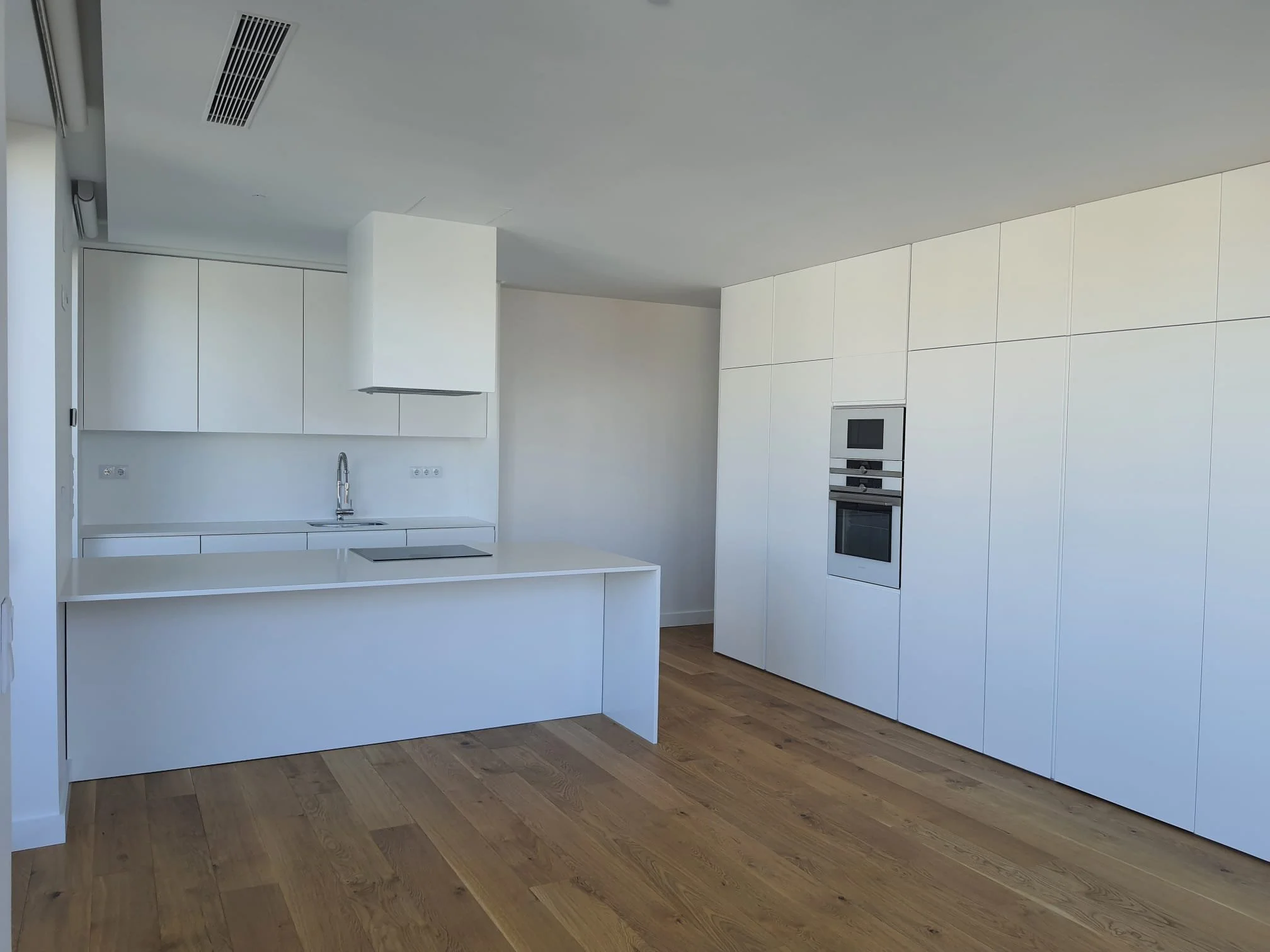 Cozinha moderna com armários brancos, eletrodomésticos embutidos e piso de madeira.