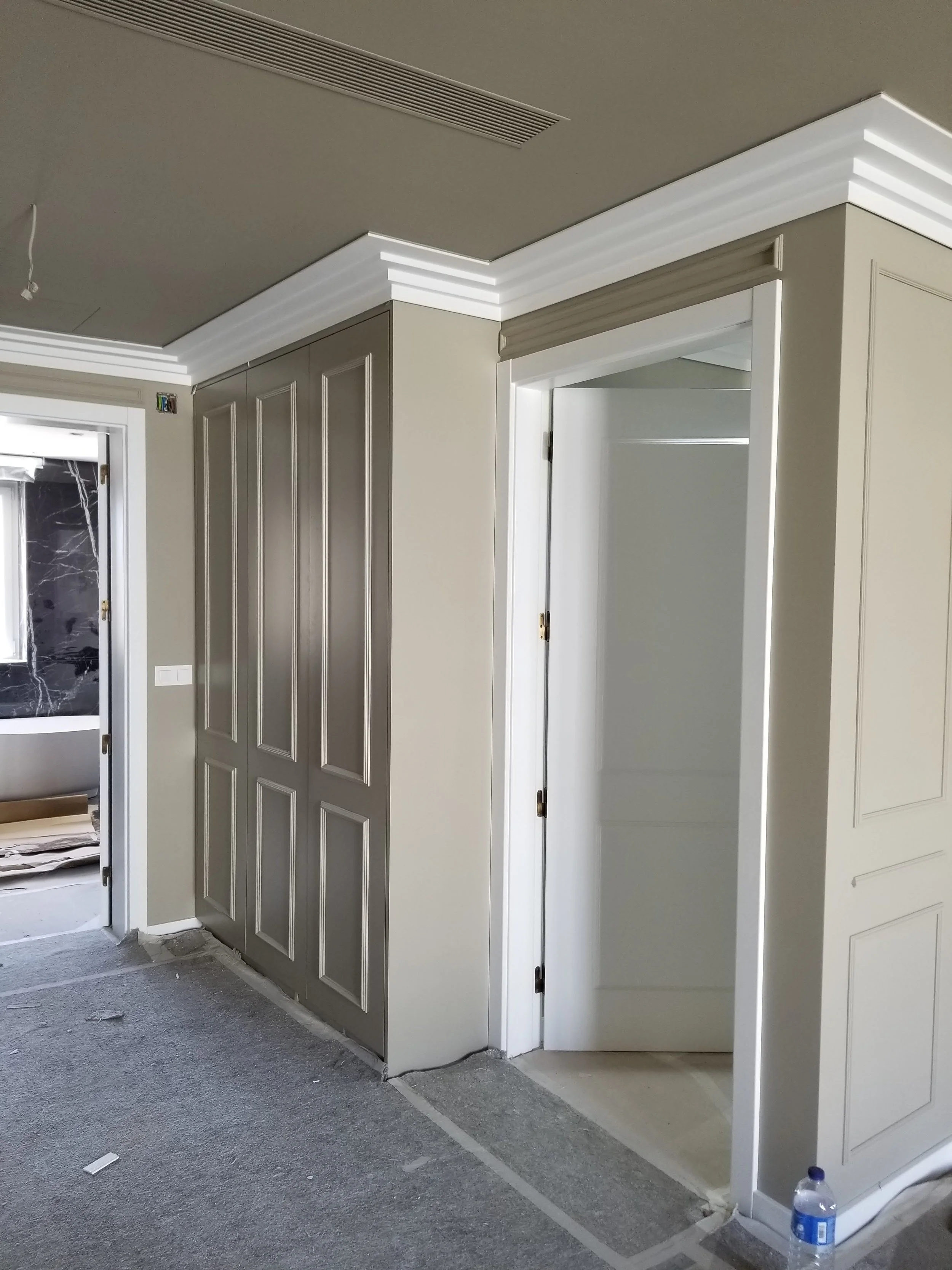 Construção de uma parede interna com porta de correr branca, detalhes de moldura e teto rebaixado com iluminação.