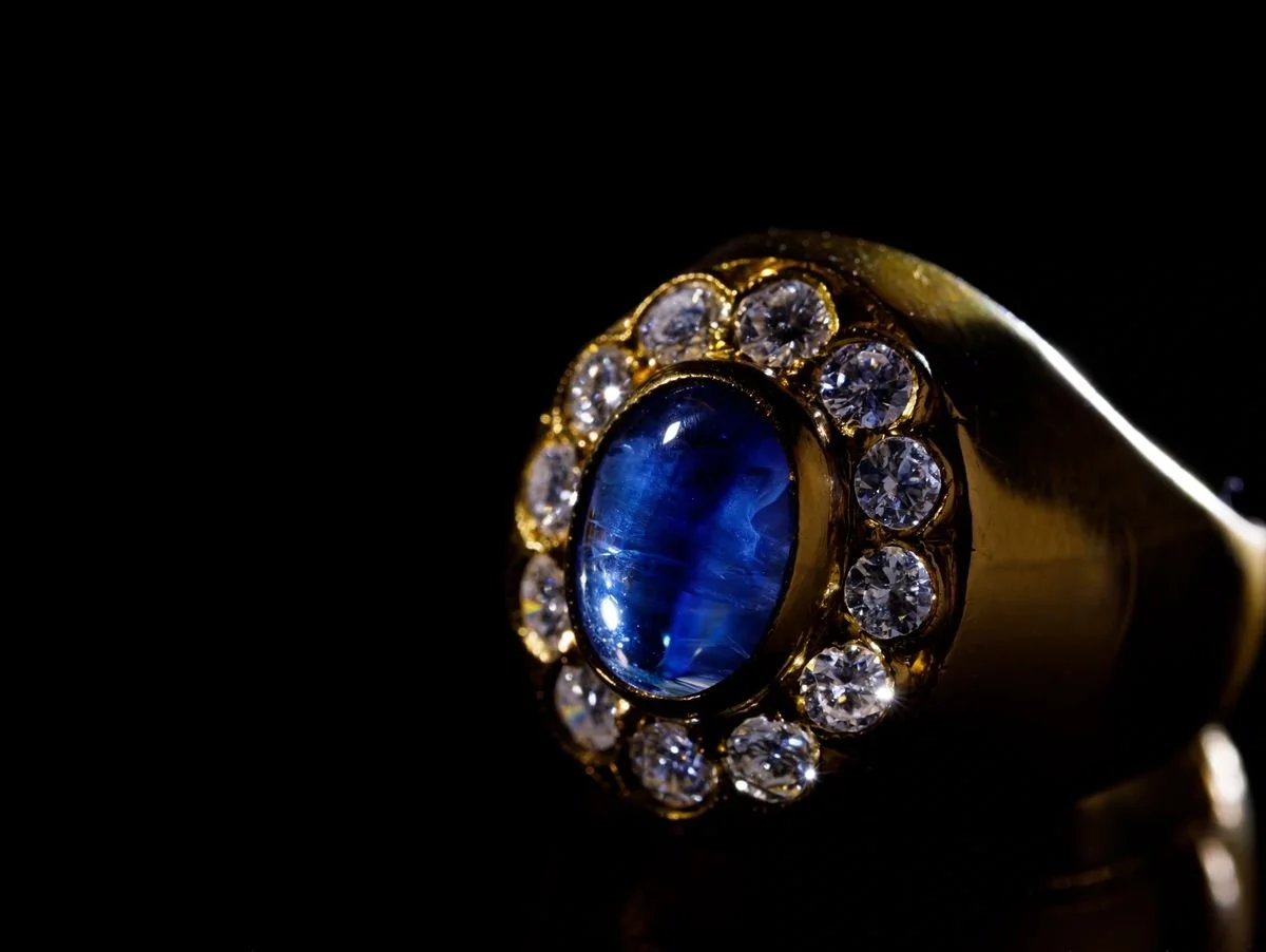 Close-up of a gold ring featuring a large blue gemstone surrounded by small diamonds on a black background.