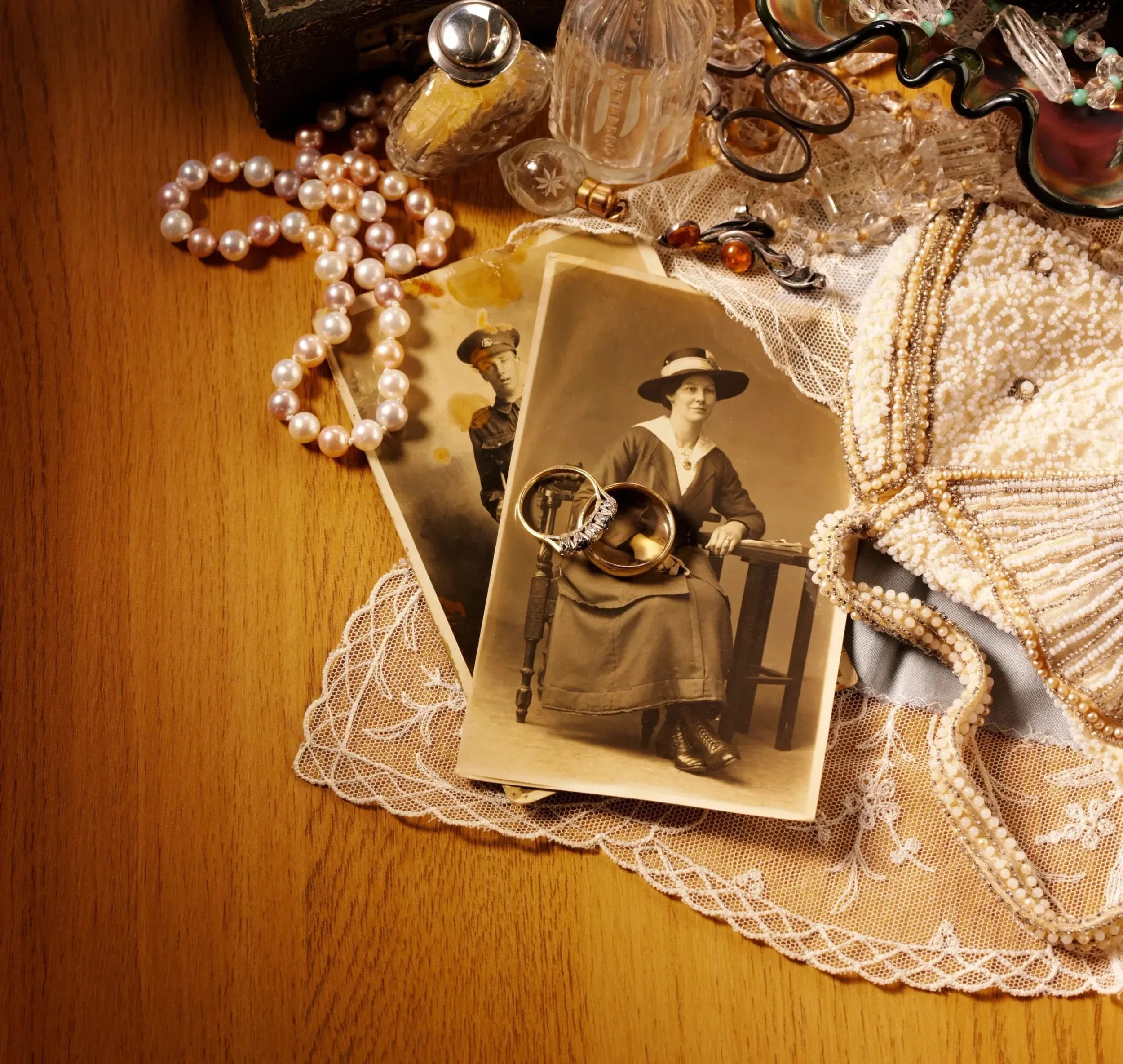 Various jewelry pieces including pearl necklaces, rings, and earrings, along with vintage photographs of women, all on a lace cloth. Jewelry appraisal and heirloom jewelry collection