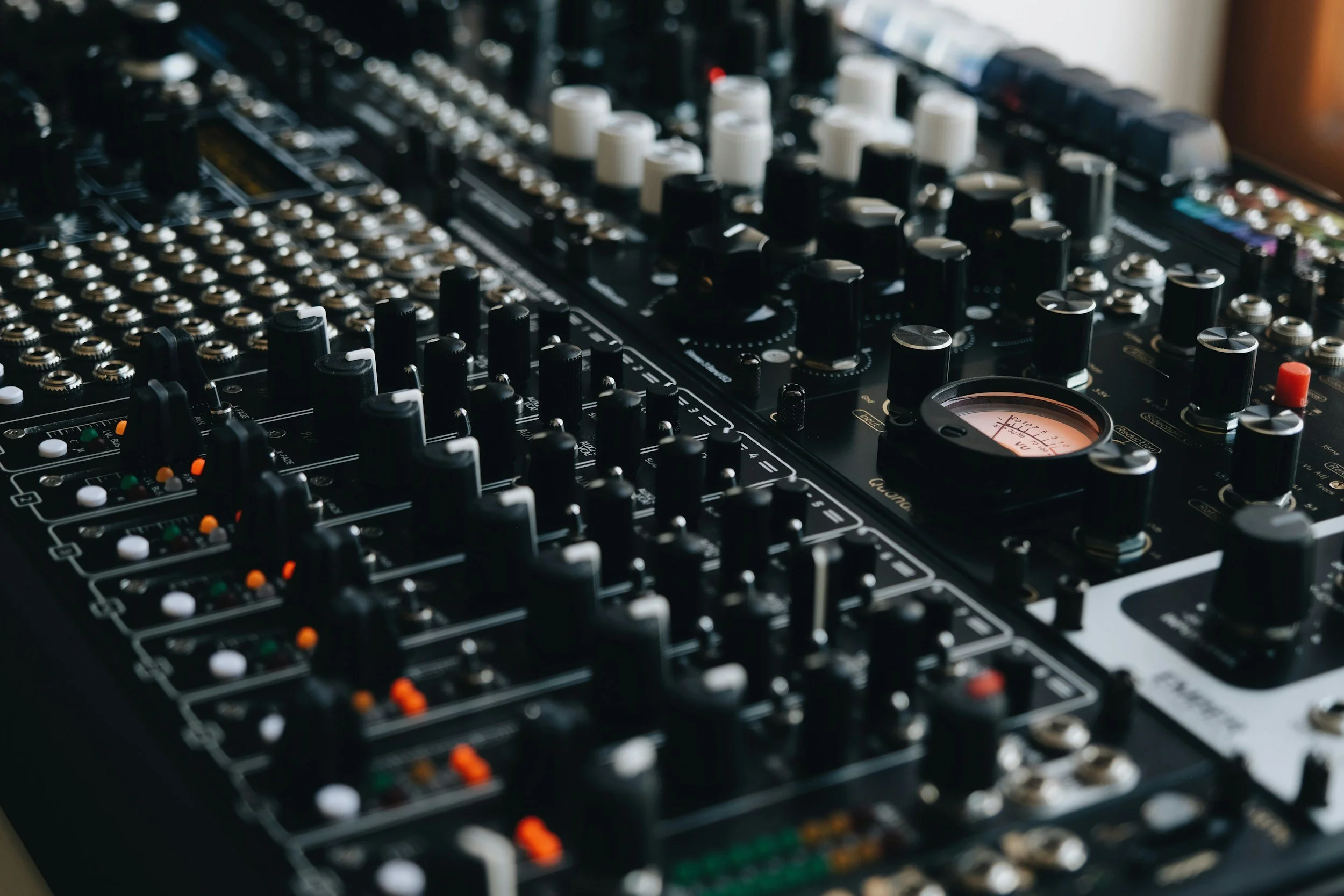 Close-up of a professional audio mixer or DJ equipment with black, white, and colorful knobs and dials.